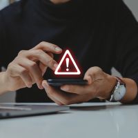 A person using a smartphone with a warning icon flashing above it.