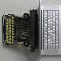 An old fashioned typewriter next to a silver laptop.