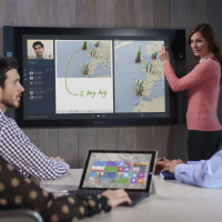 People in a conference room using a large touchscreen, called a Surface Hub, to display information.