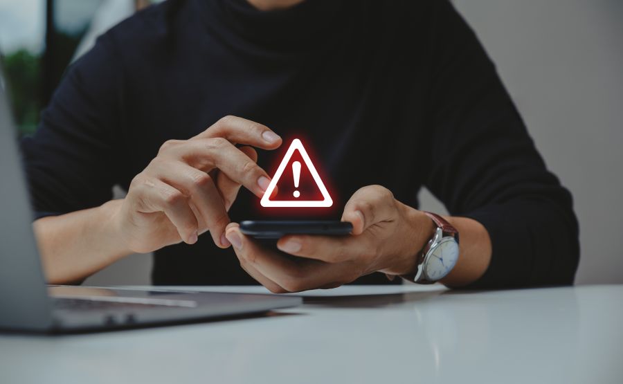 A person using a smartphone with a warning icon flashing above it.