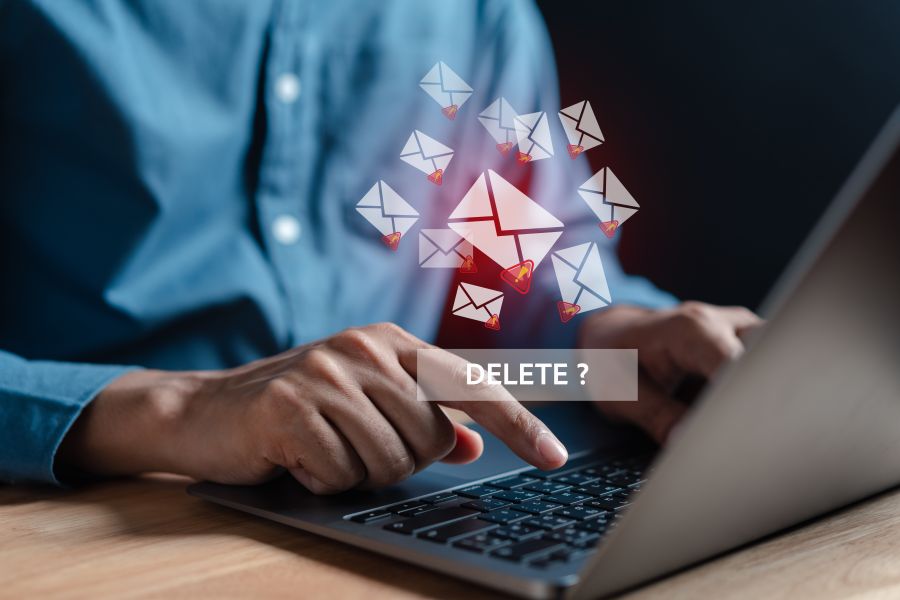 A person at a laptop with email icons floating around them. The person's finger is hovering over the Delete button.