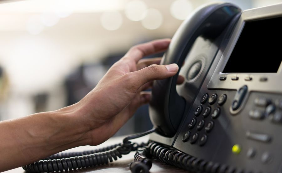 A person's hand reaching out to pick up a handset on a desk phone.