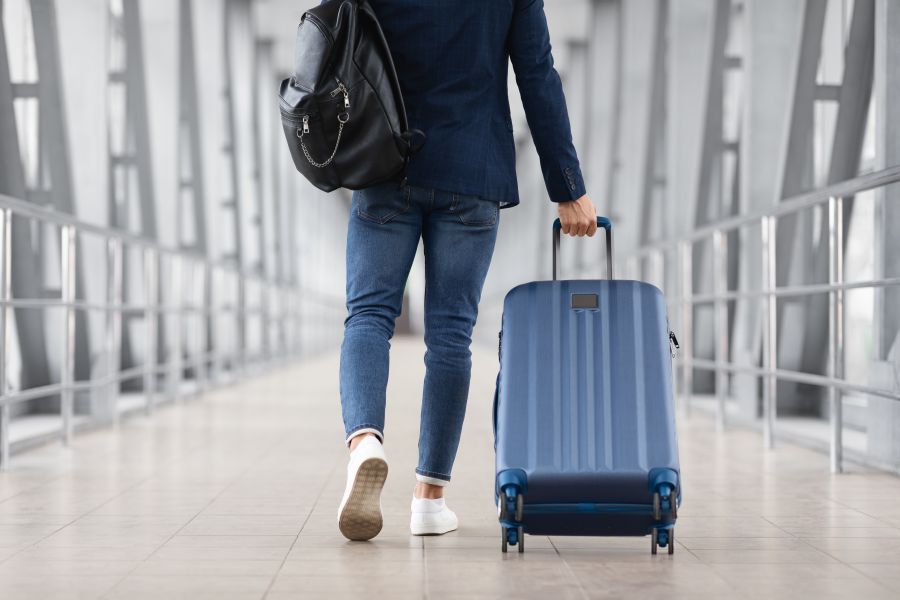 Person walking through an airport terminal while pulling a wheeled suitcase behind them