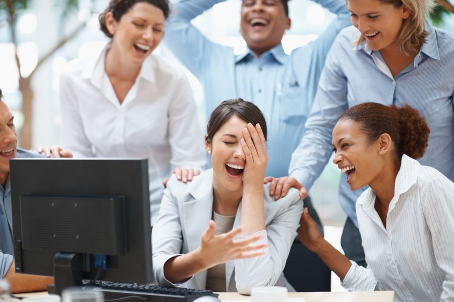 A group of people laughing in front of a computer. 