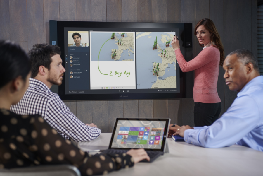 People in a conference room using a large touchscreen, called a Surface Hub, to display information.