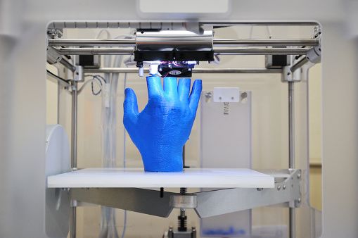A blue hand being printed in a 3D printer.