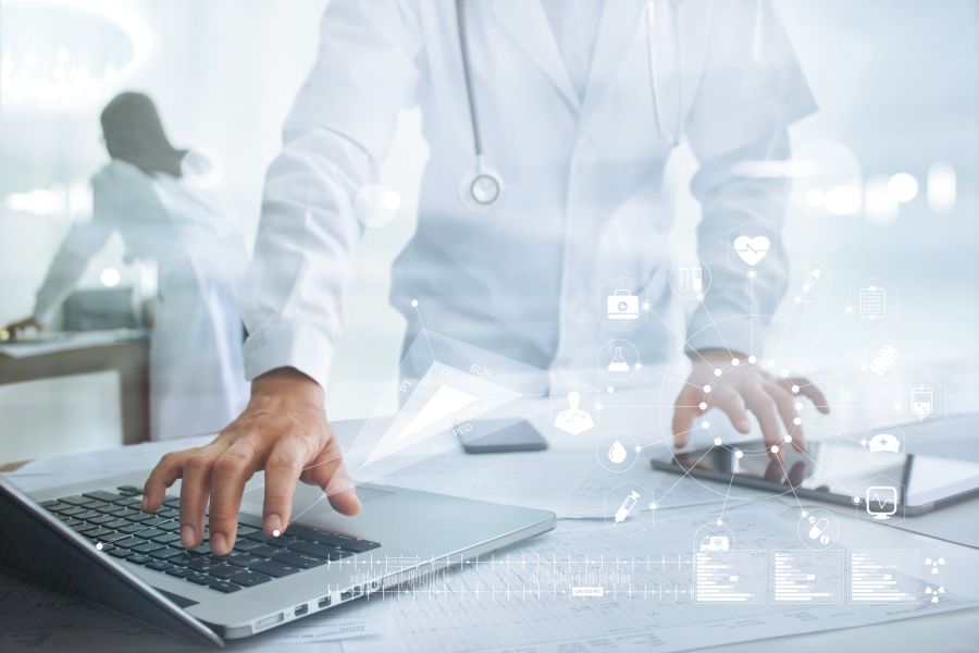 A physician using a laptop and tablet with data visualizations superimposed over the image.