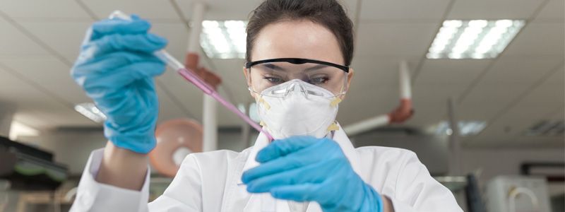 Female lab technician wearing PPE, using lab equipment to conduct research.