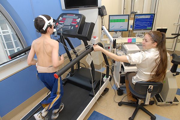 Young patient on treadmill receiving rehabilitation therapy, as a physician observes.