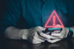 A pair of hands holding a smartphone. A warning notification hovers above the phone.